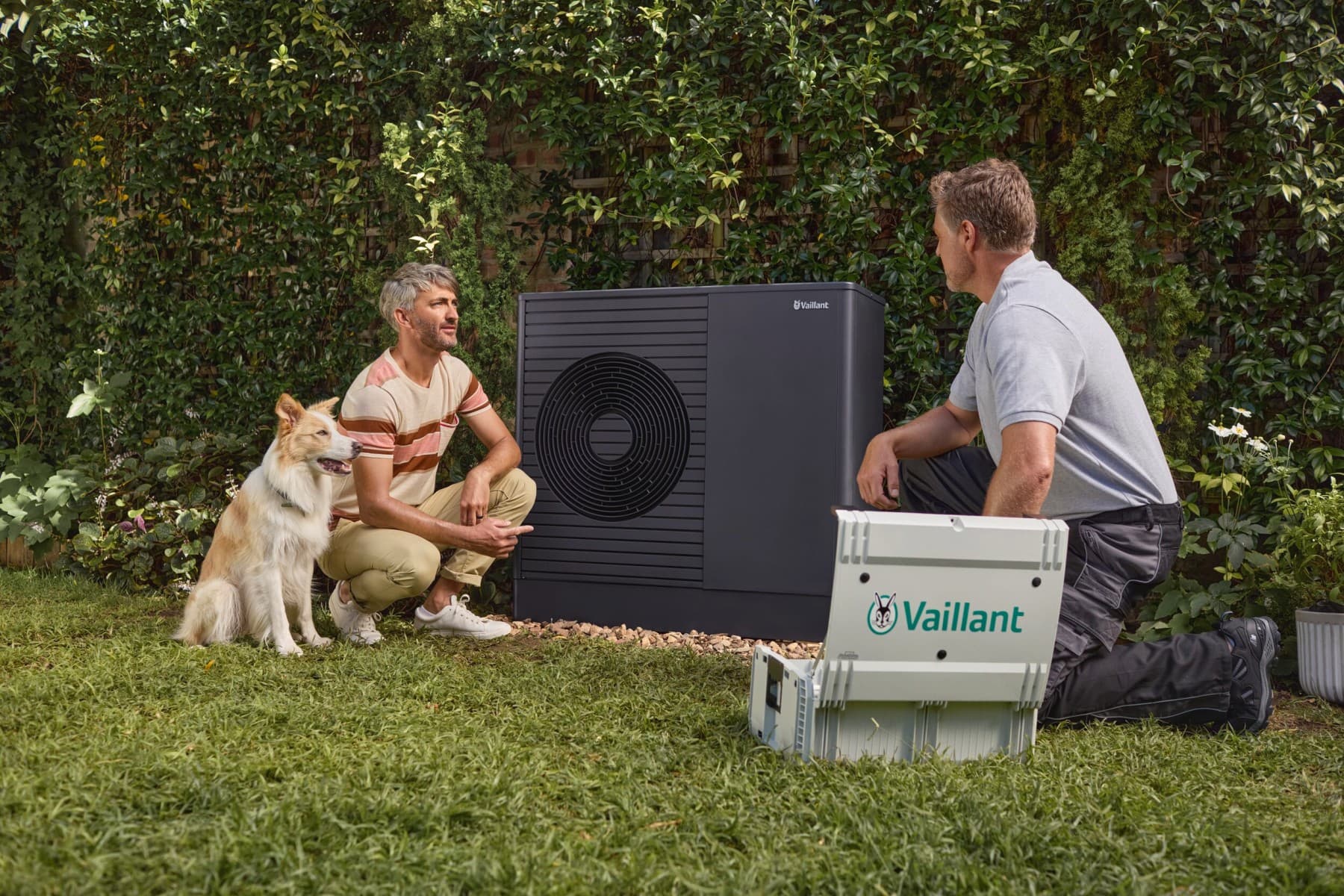Um instalador está agachado em frente a uma bomba de calor e explica algo a um homem.